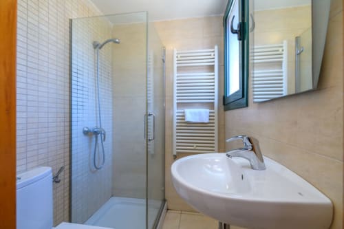 Modern bathroom with corner shower, white pedestal sink, heated towel rail, and mirror in Cal Metge cottage at Rural Montseny