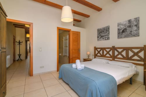 Spacious bedroom at Rural Montseny cottage with wooden-framed bed, white linens, beamed ceiling, and en-suite bathroom in