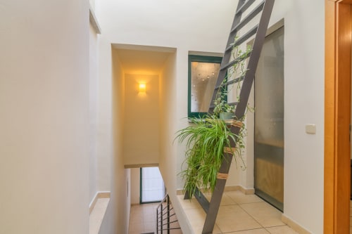 Modern hallway at Rural Montseny cottage with white walls, wooden staircase, potted plant, and warm lighting