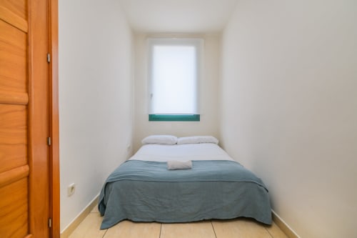 Compact bedroom at Rural Montseny cottage with double bed, white pillows, blue blanket, wooden door, and window with mountain