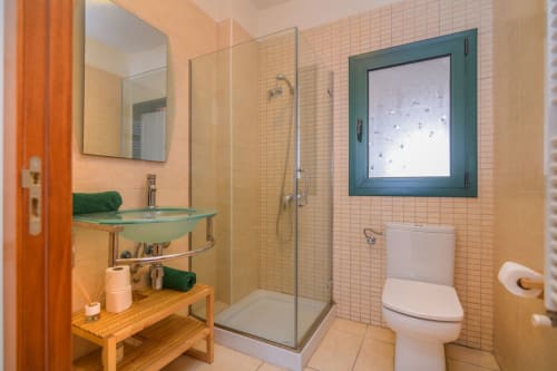 Modern bathroom with glass shower, green sink, and teal-framed window at Rural Montseny cottage in Gualba