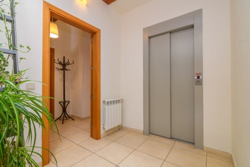 Modern hallway with elevator doors, green plant, and coat rack in Cal Metge cottage at Rural Montseny hotel, Gualba
