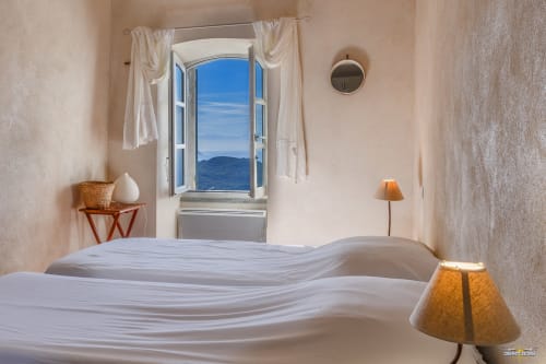 Chambre lumineuse à la Villa Cecile de La Conciergerie du Cap Corse avec vue mer par fenêtre ouverte, lits blancs et atmosphère chaleureuse
