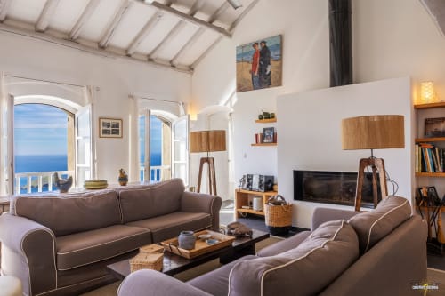 Lumineux séjour de villa méditerranéenne avec vue mer, canapés marron, accents bois et balcon surplombant Centuri, Corse