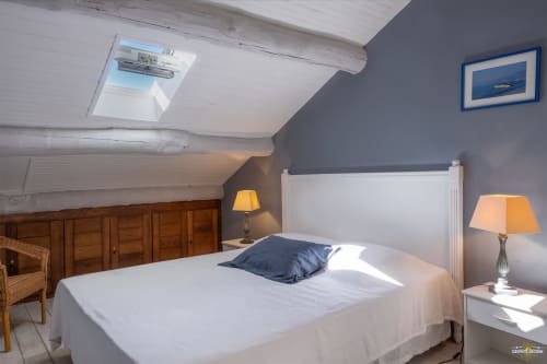 Chambre lumineuse sous les toits à la Villa CECILE à Centuri avec puits de lumière, lit blanc, murs bleus et décor nautique