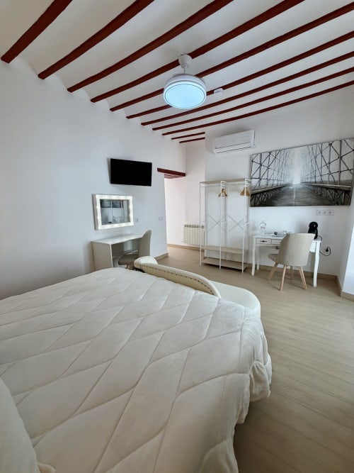 Modern bedroom with white bedding, exposed wood beams, desk, and bridge artwork at Retiro del Teatro, Almagro
