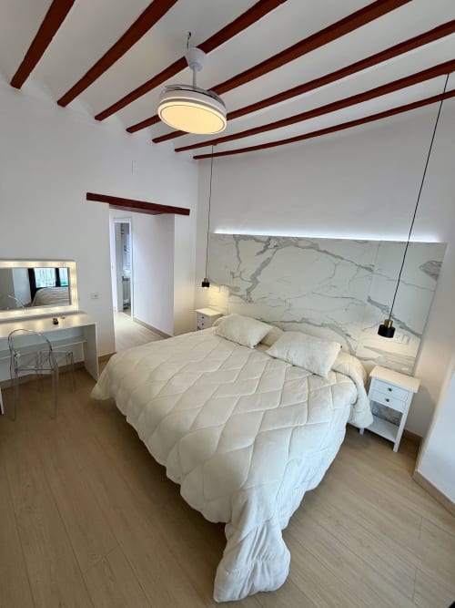 Modern bedroom at Complejo Turístico Retiro del Teatro with marble headboard, ceiling fan, vanity desk, and wooden beams