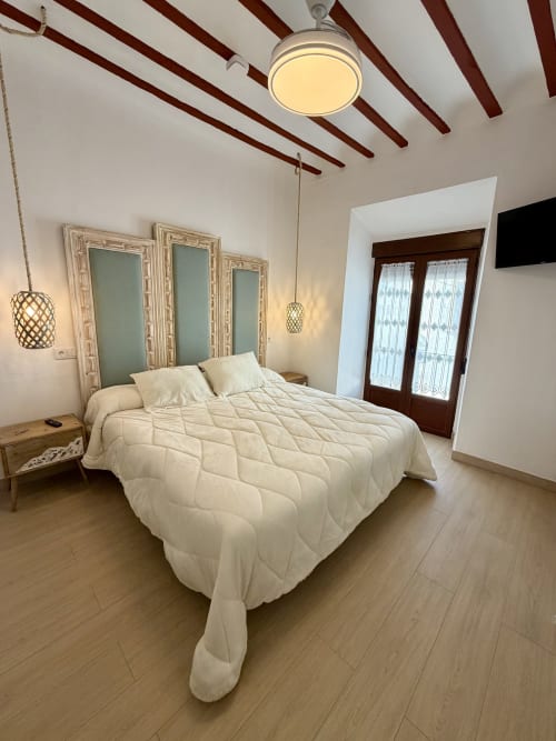 Modern bedroom at Complejo Turístico Retiro del Teatro with cream bedding, exposed beams, mirror headboard, and pendant