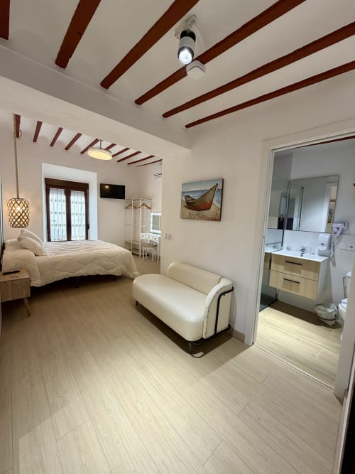 Modern bedroom at Retiro del Teatro, Almagro with queen bed, cream bench, en-suite bathroom, wooden beams, and TV