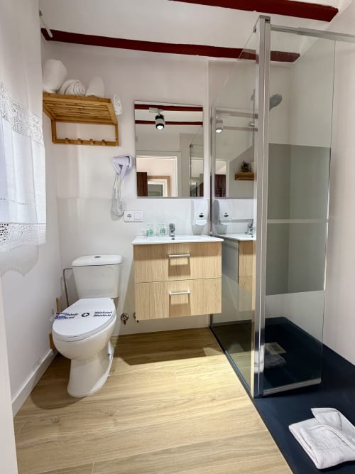 Modern bathroom in Room 204 at Retiro del Teatro with wooden vanity, glass shower, toilet, and beige tile flooring
