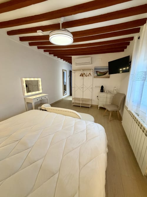 Modern bedroom at Retiro del Teatro in Almagro with queen bed, lit vanity mirror, TV, and exposed wooden ceiling beams