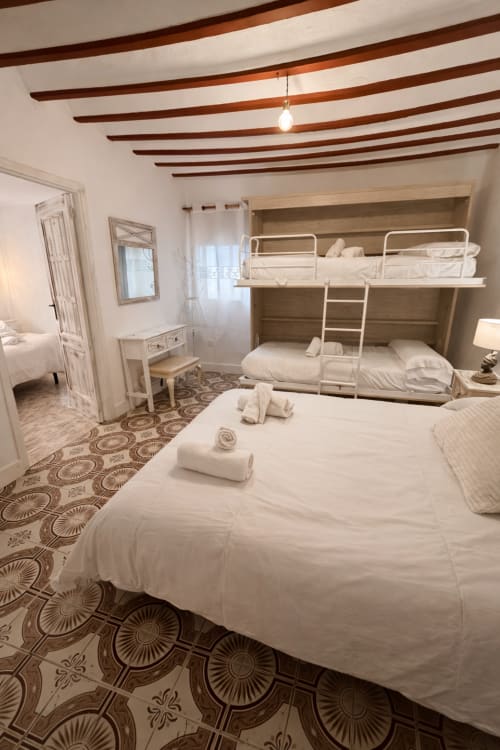 Habitación luminosa con literas, techo de vigas de madera, piso de azulejos decorados y toallas enrolladas en Retiro del Teatro