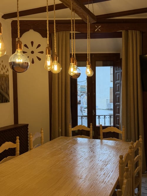 Elegante comedor en Villa Corral de Comedias con luces colgantes, mesa de madera y vista al balcón del hito de Almagro