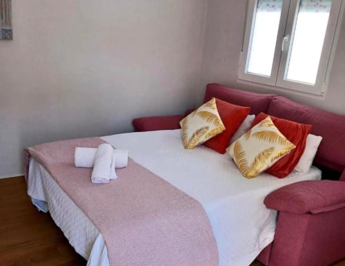 Acogedora habitación en apartamento de Mérida con cabecero burdeos, sábanas blancas, cojines decorativos y toallas enrolladas.