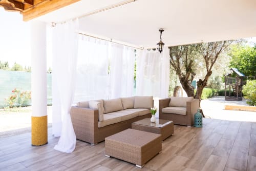 Covered patio with wicker seating, white curtains, and olive trees at Finca Navalpino, a charming bed and breakfast in
