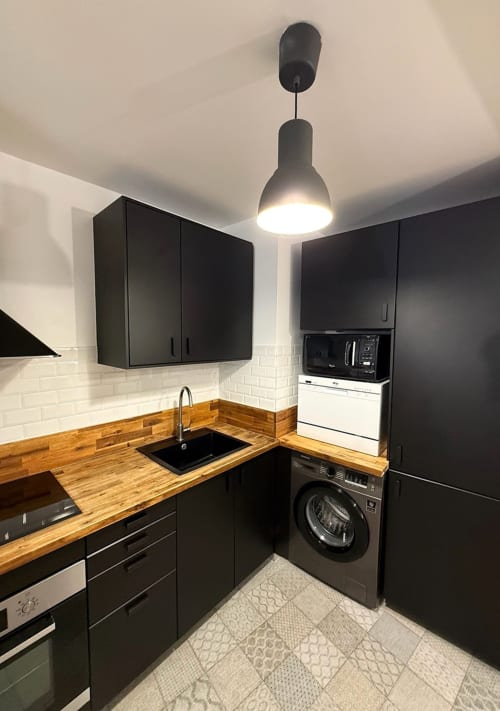 Cuisine moderne avec armoires noires, comptoirs en bois, dosseret en carrelage blanc et électroménagers en acier inoxydable