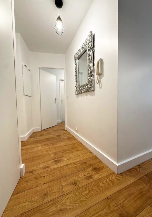 Couloir moderne de la Résidence Disneyland Place Toscane avec murs blancs, parquet, miroir ornementé et luminaires suspendus