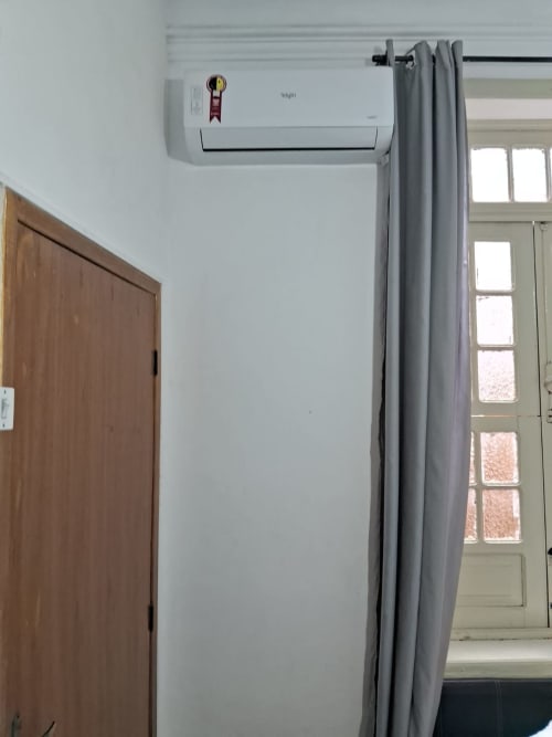 Ar condicionado Elgin split instalado em parede branca na suíte do Rio Vibes Hostel com cortinas cinzas e porta de madeira