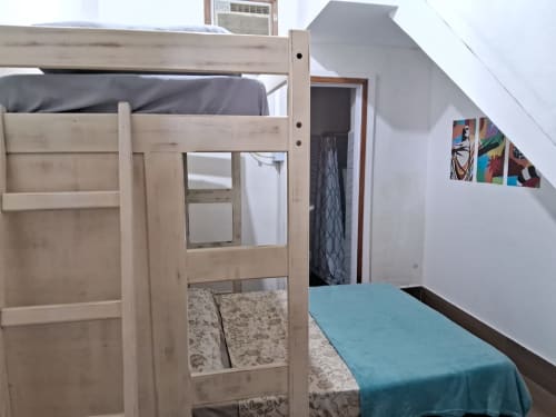 Cama alta em madeira em uma espaçosa Triple Suite do hostel Rio Vibes no Rio de Janeiro, com roupa de cama turquesa e paredes brancas.