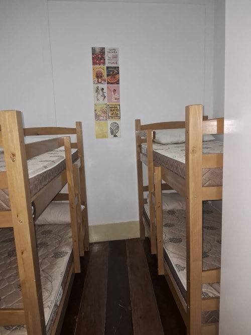 Quarto dormitório misto no Rio Vibes Hostel com camas beliche de madeira, piso com padrões e pôsteres de cultura brasileira em fundo branco
