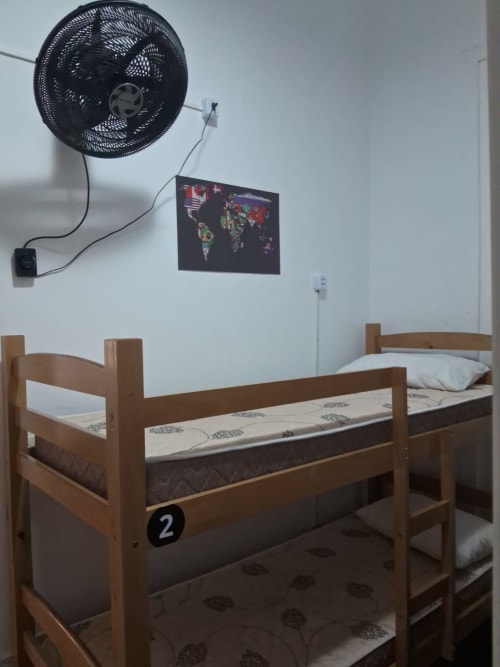 Quarto dormitório compartilhado no Rio Vibes Hostel com beliches de madeira, ventilador, pôster com mapa-múndi e móveis básicos no Rio de