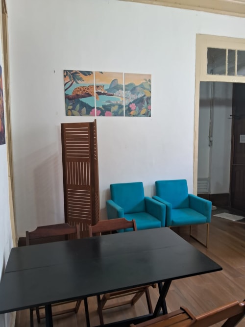 Área comum moderna no Rio Vibes Hostel com cadeiras turquesas, mesa de jantar e arte tropical com vista para o Rio de Janeiro