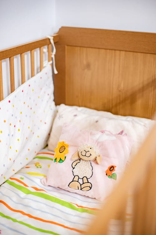 Cozy wooden baby crib at Finca Navalpino with colorful bedding, stuffed bear, and flower toys in Guadamur