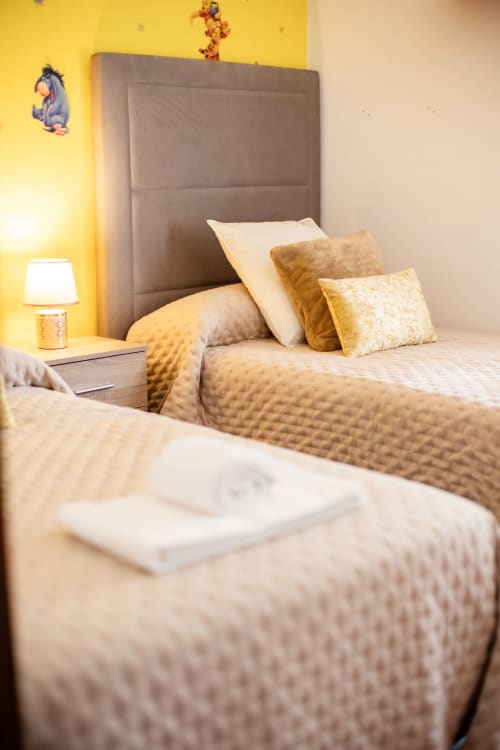 Acogedora habitación en Finca Navalpino con pared de acento amarillo, cabecero tapizado y almohadas doradas en Guadamur, España