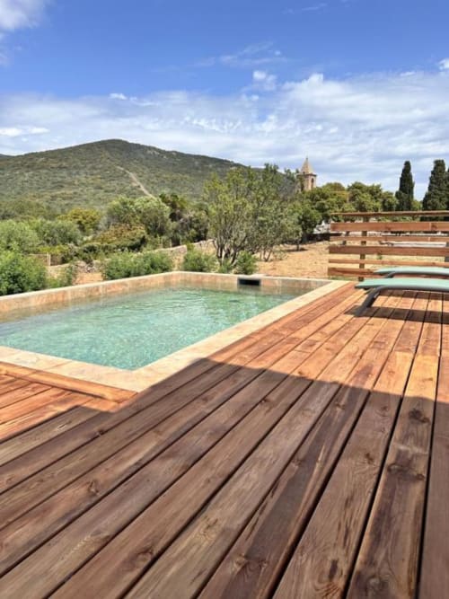 Piscine avec terrasse en bois surplombant les collines de Figari et l'église à l'hôtel In Casa Conciergerie