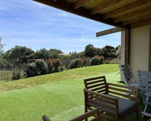 Expansive green lawn with wooden lounge chairs under pergola, overlooking hedged garden at In Casa Conciergerie, Figari