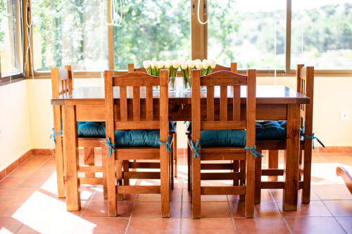 Wooden dining table with white tulips at Finca Navalpino, Guadamur, with countryside views through large windows.