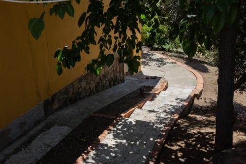 Shaded garden pathway at Finca Navalpino with benches, yellow wall, and verdant vegetation in Guadamur