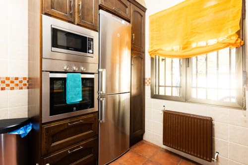 Modern kitchen at Finca Navalpino B&B in Guadamur with stainless steel appliances, wood cabinets, and bright window.