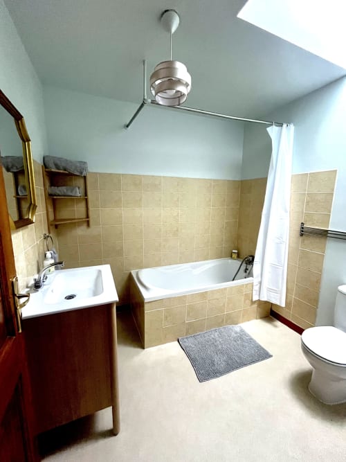 Salle de bain moderne au Manoir de Fornebello avec murs en carrelage beige, baignoire blanche, lavabo sur pied et ventilateur contemporain