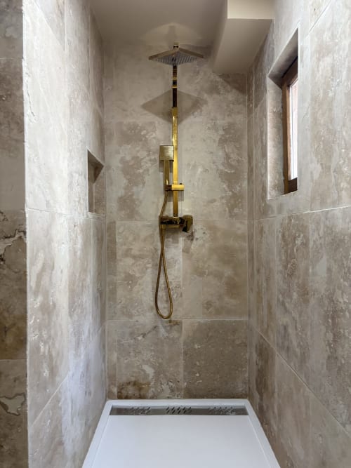 Douche moderne avec robinetterie laiton et tête de douche cascadante dans salle de bain d'appartement à Arles aux murs en travertin