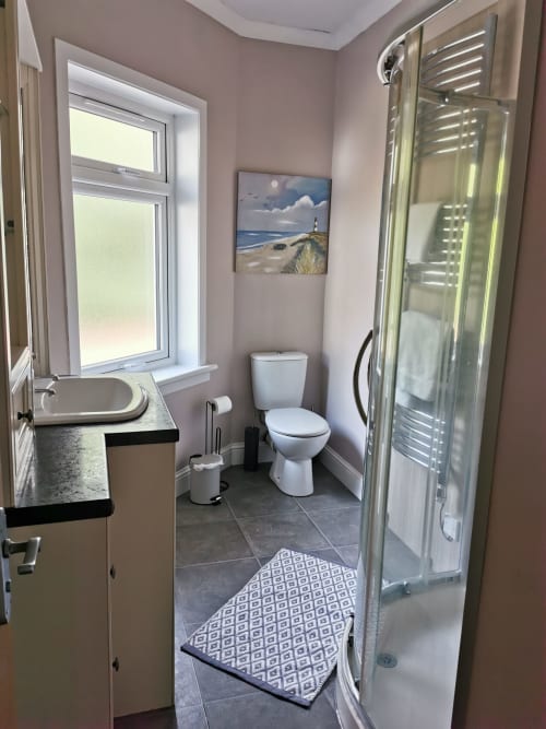 Modern bathroom at Arrochoile Glasgow B&B with sink, toilet, shower enclosure, window, and coastal artwork