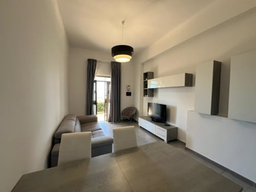 Soggiorno moderno in appartamento fronte mare con divano grigio, TV, zona pranzo e vista sul mare a Marina di Strongoli