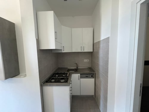 Cucina compatta in appartamento fronte mare a Marina di Strongoli con mobili bianchi, fornello a gas, lavello e rivestimento grigio