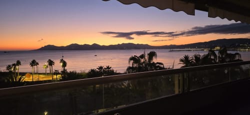 Vista al tramonto sul mare dal balcone dell'appartamento La Dolce Vita con palme e costa mediterranea
