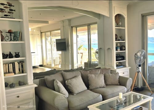 Luminoso soggiorno costiero con divano grigio, librerie bianche integrate, porte con vista mare e comfort moderni a La Dolce Vita