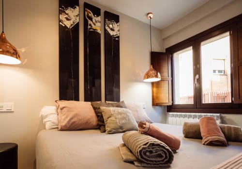 Dormitorio moderno del hotel Unique Rooms Burgos con cama, lámparas colgantes de cobre, obras de arte oscuro y toallas enrolladas.