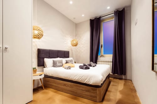 Dormitorio moderno en Loft Center Burgos con cama de madera, cabecero oscuro, luces colgantes doradas y vistas a la ciudad