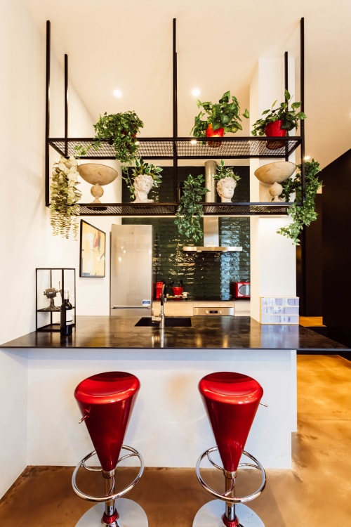 Cocina loft moderna en Burgos con taburetes rojos, encimera negra y sala de estar con plantas en maceta y esculturas