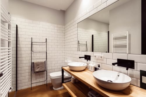 Baño moderno con dos lavabos de cerámica sobre tocador de madera, azulejos tipo metro, herrajes negros y ducha tipo walk-in en Loft Center