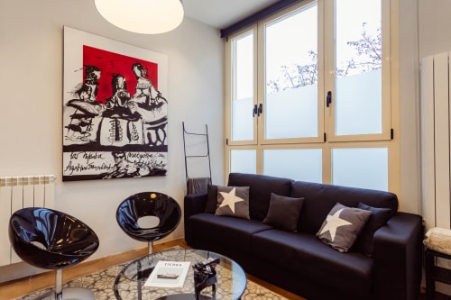 Sala de estar tipo loft moderno en Burgos con sofá negro, cojines de estrellas, arte contemporáneo y amplias ventanales con vistas a la ciudad