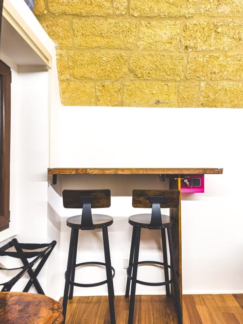 Bancone bar moderno con top in legno e due sgabelli neri nell'appartamento CorteLirice Paradiso, muro in mattoni gialli