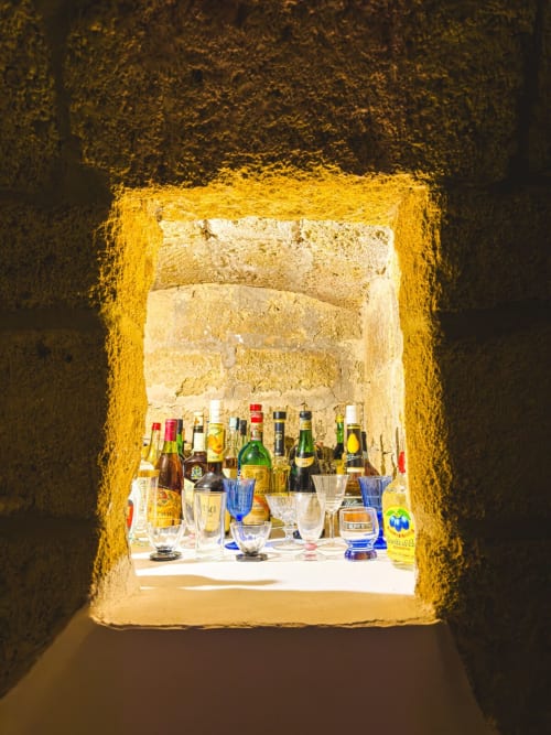 Bottiglie di vino e bicchieri esposti attraverso una porta in pietra con cornice gialla presso l'appartamento CorteLirice Paradiso, Italia