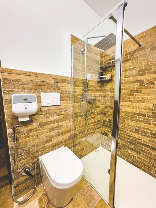 Bagno moderno con pareti in mattoni dorati, toilette bianca e doccia in vetro all'appartamento CorteLirice Paradiso
