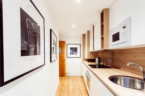 Cocina abierta moderna del apartamento Five Senses en Burgos con muebles de madera, fregadero de acero inoxidable y obra contemporánea
