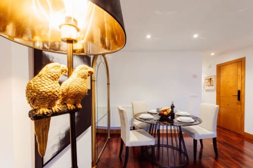 Elegante zona de comedor en apartamento de Burgos con lámpara de loro dorado, mesa redonda y pisos de madera